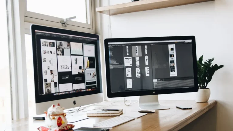 Bright web design workspace with two desktop monitors showing website layouts